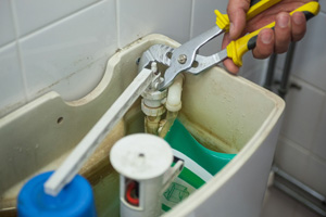 Close up of hand repairing toilet with pliers