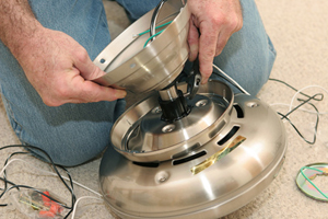 An electrician assembling a ceiling fan motor. All work is being performed by a licensed master electrician according to National Electric Code standards.